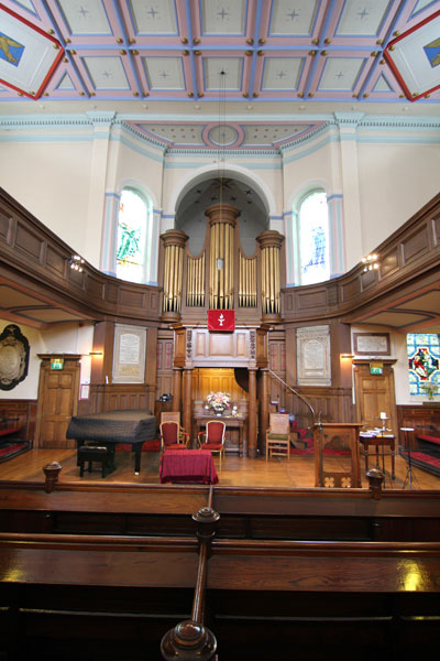 Chancel Platform with Grand Piano to the left and 'Truth' and 'Liberty' windows either side of the organ pipes.  The Chapel has excellent acoustics.